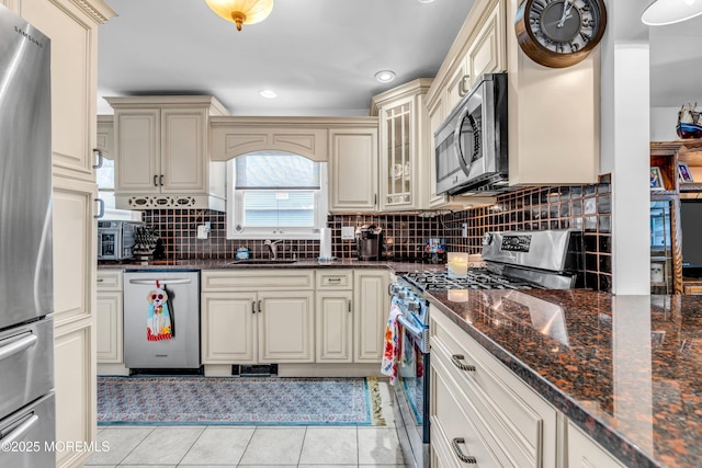 kitchen with sink, dark stone countertops, light tile patterned floors, stainless steel appliances, and cream cabinetry