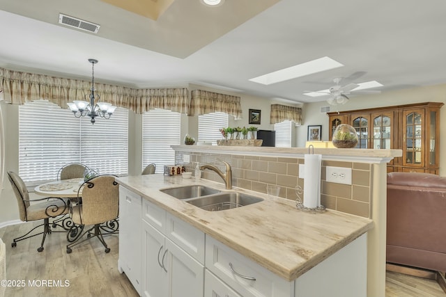 kitchen with sink, light hardwood / wood-style flooring, hanging light fixtures, a skylight, and white cabinets