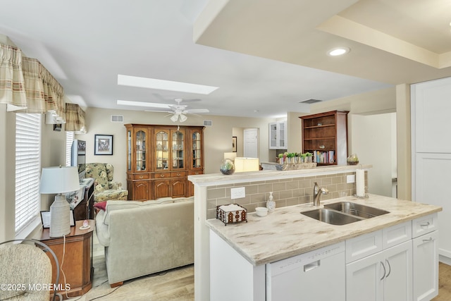 kitchen featuring sink, a skylight, white dishwasher, decorative backsplash, and white cabinets