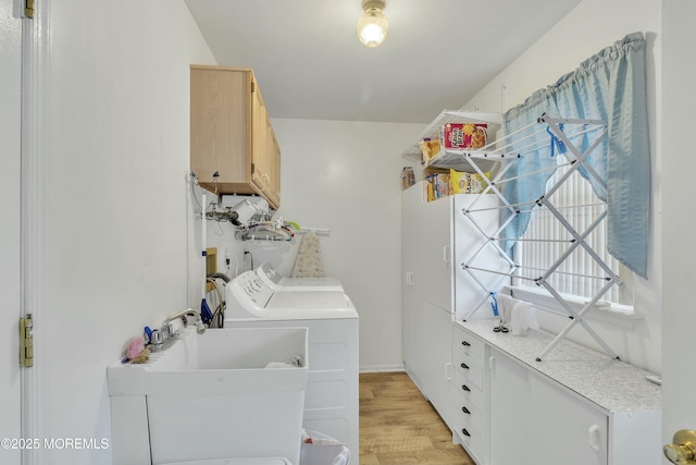 laundry area with light hardwood / wood-style floors, sink, washing machine and dryer, and cabinets