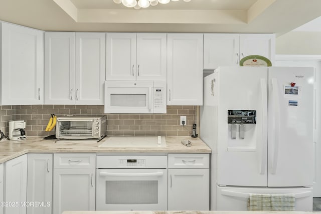 kitchen featuring tasteful backsplash, light stone counters, white cabinets, and white appliances