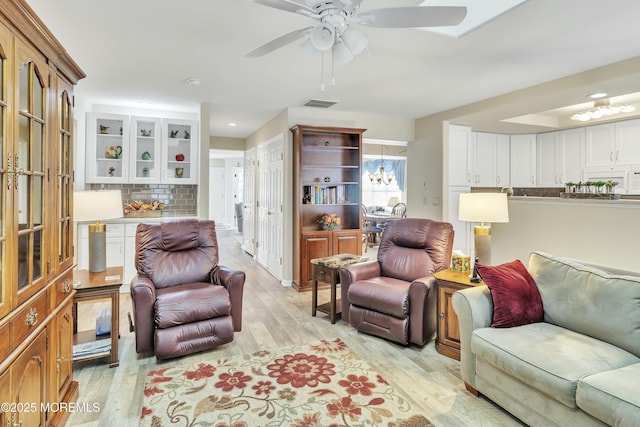 living room featuring ceiling fan with notable chandelier and light hardwood / wood-style floors