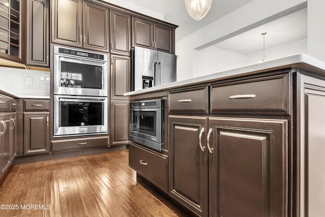 kitchen featuring crown molding, dark wood-type flooring, appliances with stainless steel finishes, dark brown cabinets, and tasteful backsplash