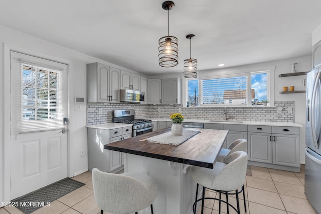 kitchen featuring decorative light fixtures, butcher block counters, sink, a center island, and stainless steel appliances