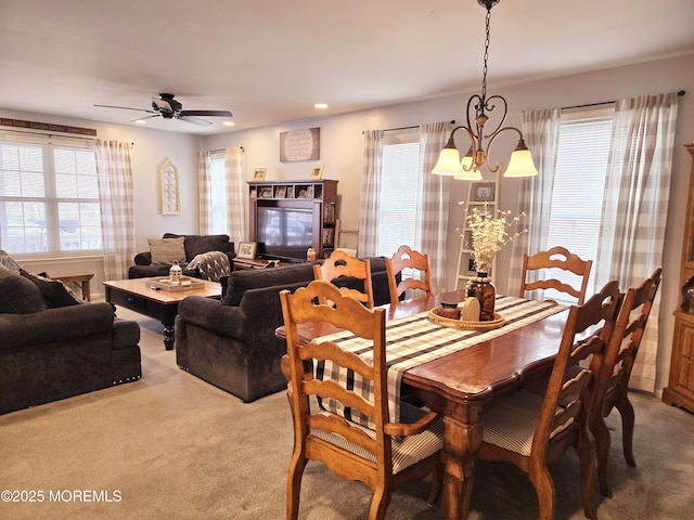 carpeted dining space featuring ceiling fan with notable chandelier and plenty of natural light