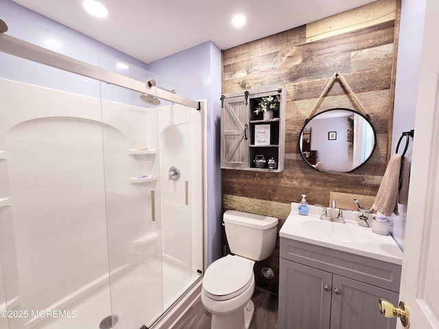 bathroom featuring vanity, toilet, a shower with door, and wood walls