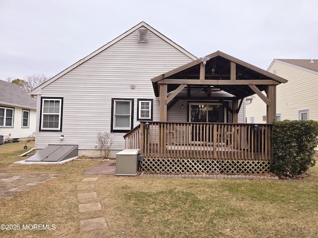 back of house featuring a wooden deck, ceiling fan, and a lawn