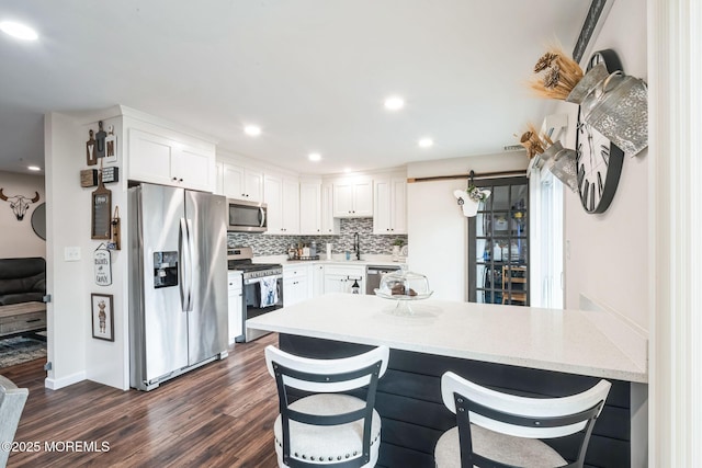 kitchen featuring backsplash, appliances with stainless steel finishes, a kitchen breakfast bar, and white cabinets