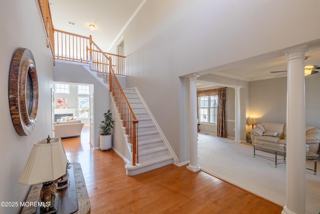 staircase featuring ornamental molding, a towering ceiling, wood-type flooring, and decorative columns