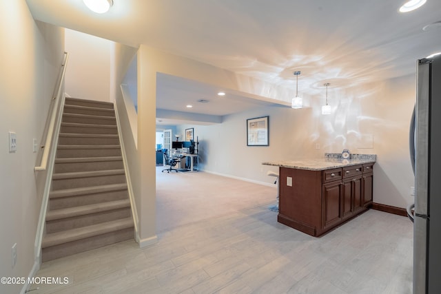 kitchen with hanging light fixtures, light stone countertops, light wood-type flooring, and stainless steel refrigerator