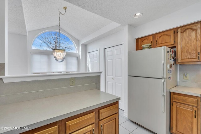 kitchen with vaulted ceiling, light tile patterned flooring, pendant lighting, white refrigerator, and a notable chandelier