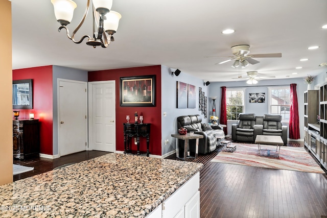 kitchen with stone counters, dark hardwood / wood-style floors, pendant lighting, ceiling fan with notable chandelier, and white cabinetry