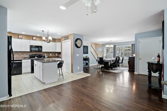 kitchen featuring white cabinetry, hanging light fixtures, a center island, black appliances, and a kitchen bar