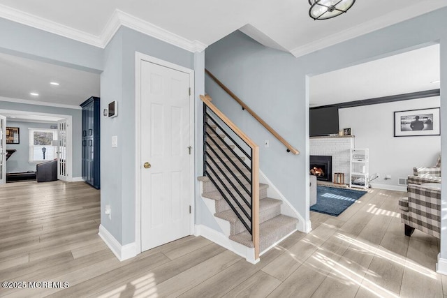 stairway featuring hardwood / wood-style flooring, crown molding, and a fireplace