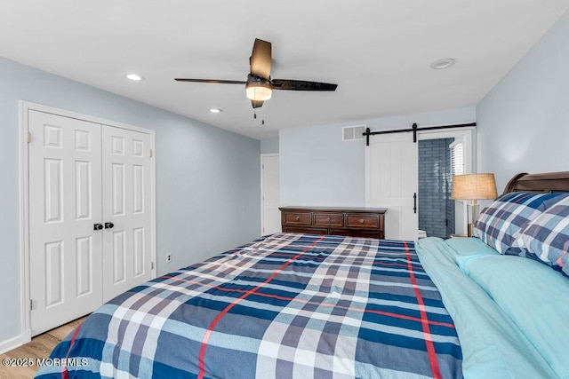 bedroom featuring a closet, light hardwood / wood-style flooring, ceiling fan, and a barn door