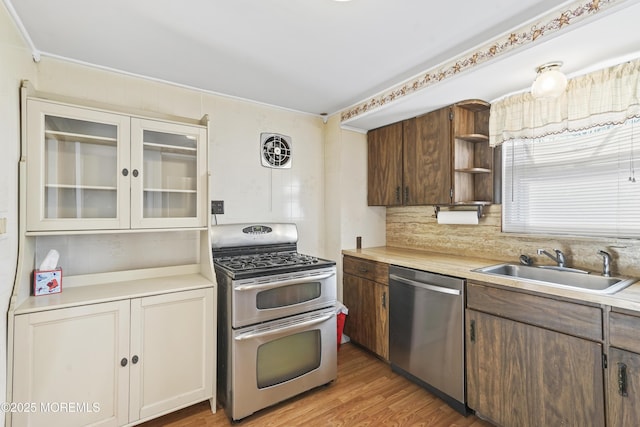 kitchen with appliances with stainless steel finishes, sink, light wood-type flooring, and decorative backsplash