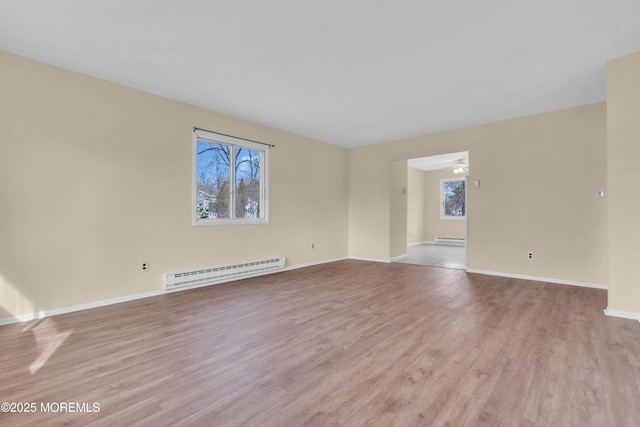 unfurnished room featuring plenty of natural light, baseboard heating, and light hardwood / wood-style floors