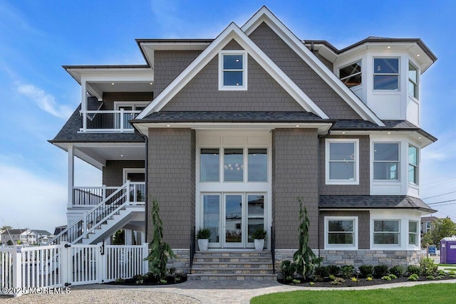 view of front of property featuring fence, stone siding, roof with shingles, and a balcony