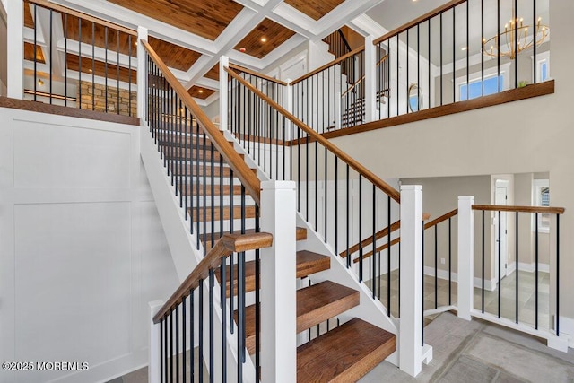 stairs featuring coffered ceiling, beam ceiling, and a towering ceiling