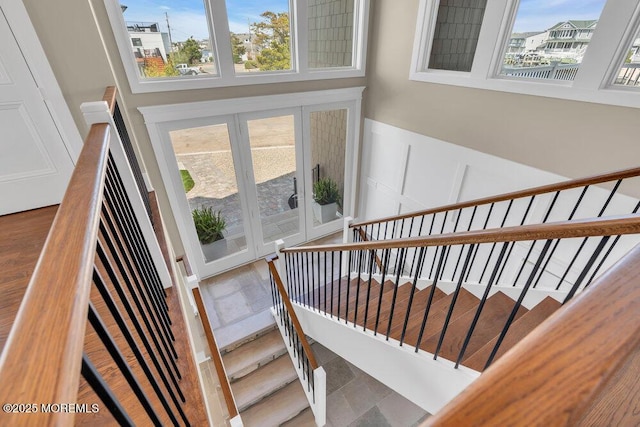 stairs featuring french doors, wainscoting, and a decorative wall