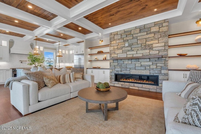 living area with a stone fireplace, coffered ceiling, wood finished floors, and beam ceiling