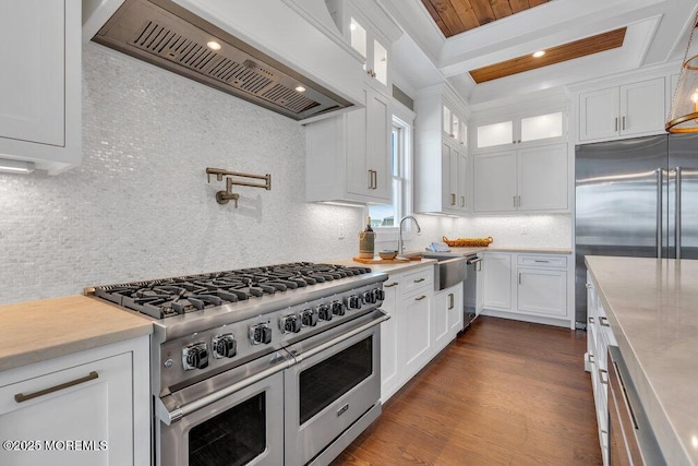 kitchen featuring custom exhaust hood, glass insert cabinets, white cabinetry, a sink, and premium appliances