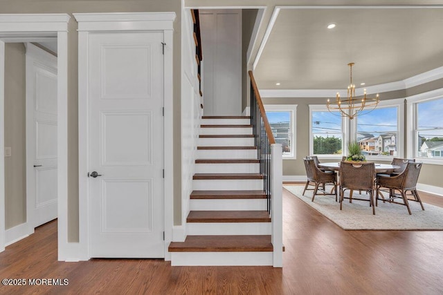stairway featuring baseboards, a chandelier, plenty of natural light, and wood finished floors