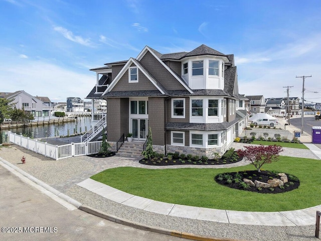 view of front facade with a water view, a front lawn, fence, and stone siding