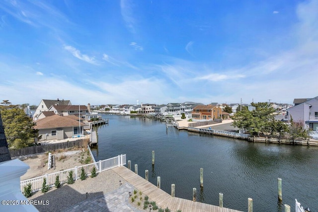 view of dock with a water view, fence, and a residential view