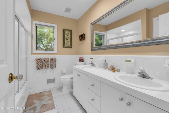 full bathroom with combined bath / shower with glass door, tile patterned flooring, tile walls, vanity, and toilet