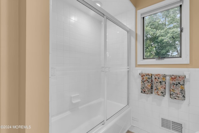 bathroom with bath / shower combo with glass door and tile walls