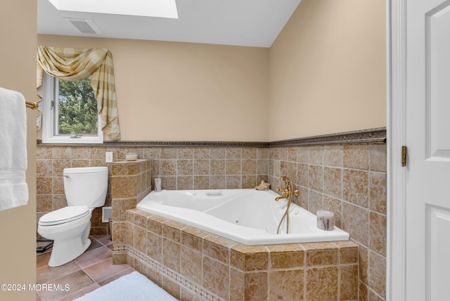 bathroom featuring a skylight, tile walls, tile patterned flooring, a relaxing tiled tub, and toilet