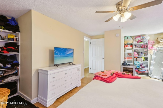 bedroom featuring light wood-style floors, baseboards, a ceiling fan, and a textured ceiling