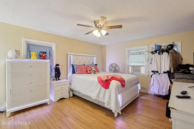 bedroom featuring light wood-style floors, ceiling fan, cooling unit, and a textured ceiling