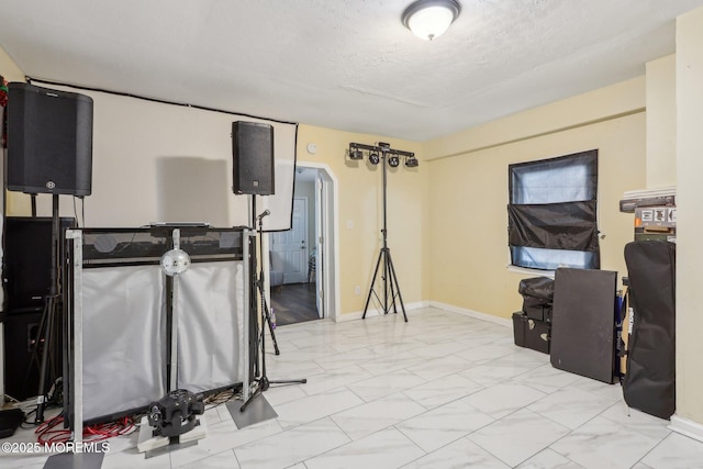 basement featuring arched walkways, marble finish floor, a textured ceiling, and baseboards