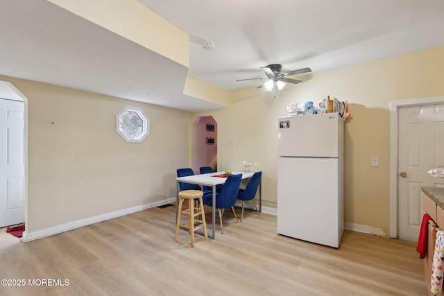 dining room featuring a ceiling fan, light wood-type flooring, arched walkways, and baseboards