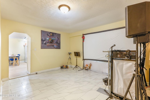 interior space featuring arched walkways, a textured ceiling, and baseboards