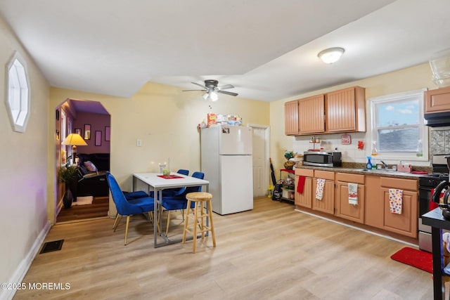 kitchen with light wood-style flooring, stainless steel appliances, visible vents, brown cabinetry, and dark countertops