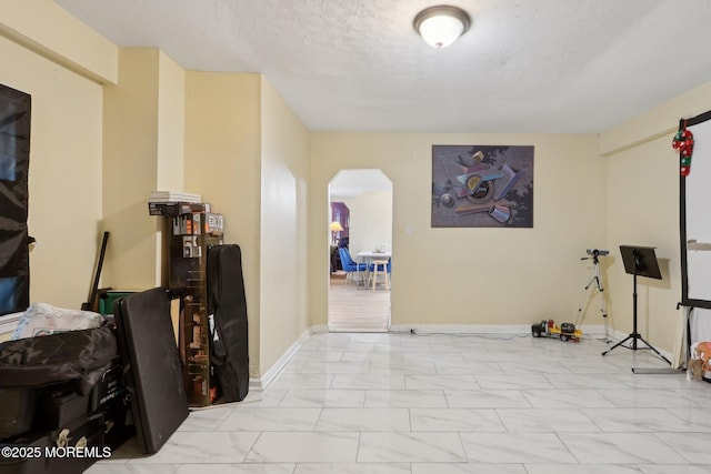 interior space featuring arched walkways, marble finish floor, a textured ceiling, and baseboards