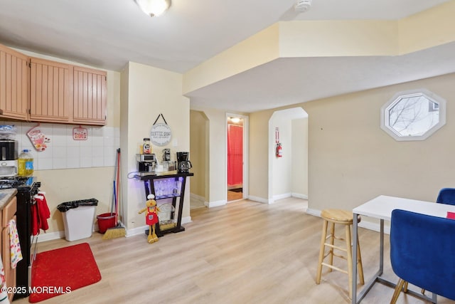 interior space with arched walkways, backsplash, gas stove, light wood-type flooring, and baseboards