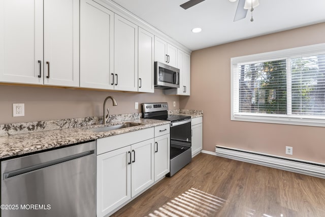 kitchen with sink, a baseboard radiator, stainless steel appliances, light stone countertops, and white cabinets