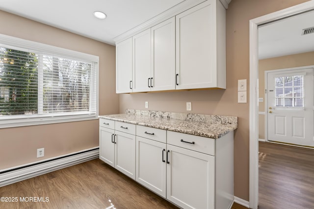 kitchen with light stone counters, a baseboard heating unit, light wood-type flooring, and white cabinets