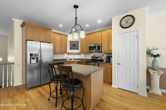 kitchen with a breakfast bar, ornamental molding, pendant lighting, stainless steel appliances, and light hardwood / wood-style floors