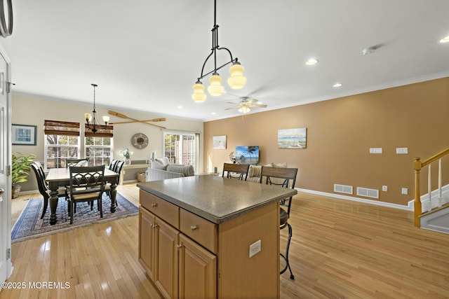 kitchen with crown molding, a kitchen breakfast bar, a kitchen island, ceiling fan with notable chandelier, and light wood-type flooring