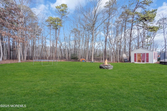 view of yard featuring a trampoline, a fire pit, and an outbuilding