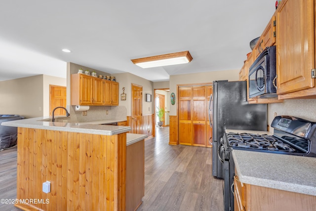 kitchen with sink, black appliances, kitchen peninsula, hardwood / wood-style floors, and backsplash