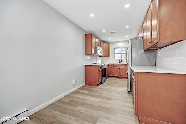 kitchen with a baseboard heating unit, stainless steel appliances, a sink, baseboards, and light wood-type flooring