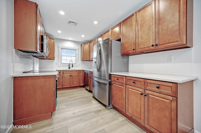 kitchen with light wood finished floors, visible vents, brown cabinetry, appliances with stainless steel finishes, and a sink