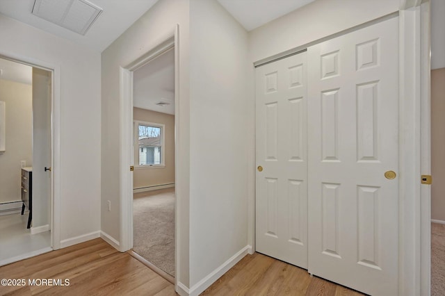 hallway with a baseboard heating unit, visible vents, light wood-style flooring, and baseboards