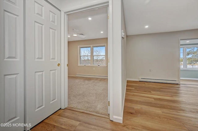 corridor with a baseboard heating unit, a baseboard radiator, wood finished floors, and a healthy amount of sunlight